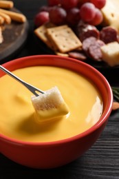 Dipping piece of bread into tasty cheese fondue at black wooden table, closeup