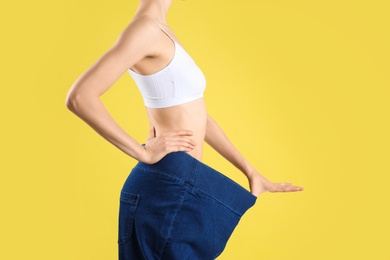 Young slim woman wearing oversized jeans on yellow background, closeup