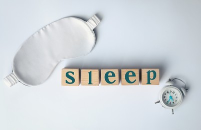 Word Sleep made of wooden cubes near blindfold and alarm clock on white background, flat lay. Insomnia treatment