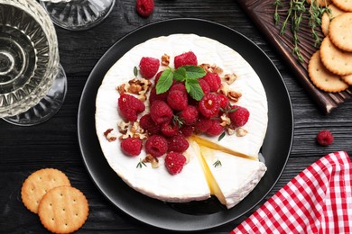 Brie cheese served with raspberries and walnuts on black wooden table, flat lay