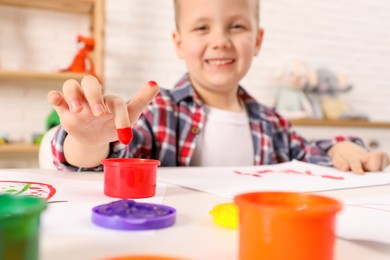 Little boy painting with finger at white table indoors, focus on hand