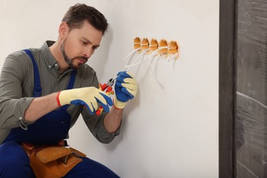 Photo of Electrician in uniform with pliers repairing power socket indoors
