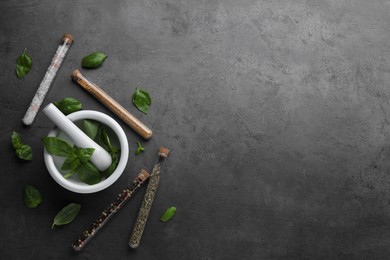 Test tubes with different spices, fresh basil leaves, mortar and pestle on grey background, flat lay. Space for text
