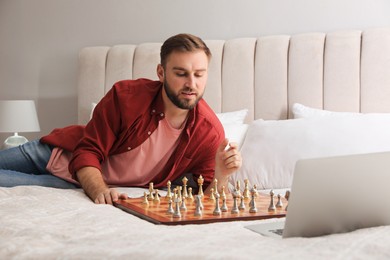 Photo of Young man playing chess with partner through online video chat on bed at home