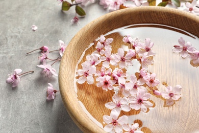 Bowl with water and blossoming flowers on grey background