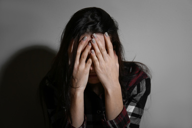 Photo of Abused young woman crying near beige wall. Domestic violence concept