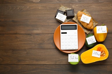 Flat lay composition of calculator and food products with calorific value tags on wooden table, space for text. Weight loss concept