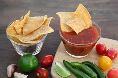 Photo of Tasty salsa sauce with tortilla chips and ingredients on wooden table, closeup