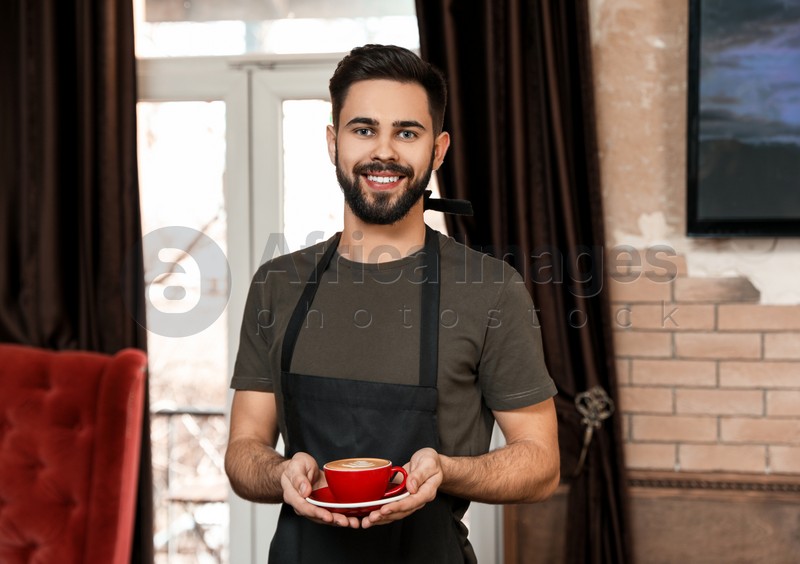 Portrait of barista with cup of coffee in shop