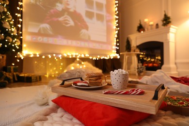 Photo of MYKOLAIV, UKRAINE - DECEMBER 24, 2020: Video projector screen displaying Home Alone movie in room, focus on tray with snack and drink. Cozy winter holidays atmosphere