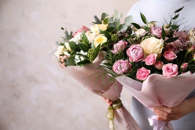 Woman with bouquets of beautiful flowers on beige background, closeup