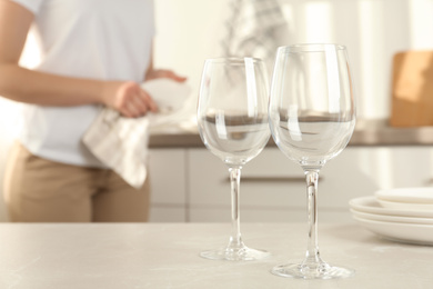 Woman wiping plate with towel in kitchen, focus on clean glasses