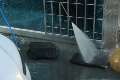 Cleaning auto mats with high pressure water jet at car wash, closeup