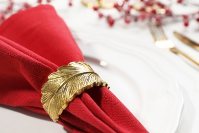 Red fabric napkin with beautiful decorative ring on white table, closeup