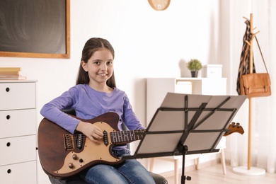 Little girl playing guitar at music lesson. Learning notes