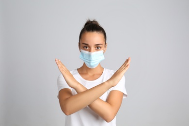 Woman in protective mask showing stop gesture on grey background. Prevent spreading of COVID‑19