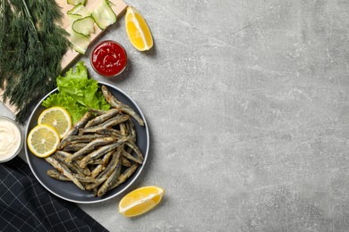 Photo of Delicious fried anchovies with lemon, lettuce leaves and sauces served on light grey table, flat lay. Space for text