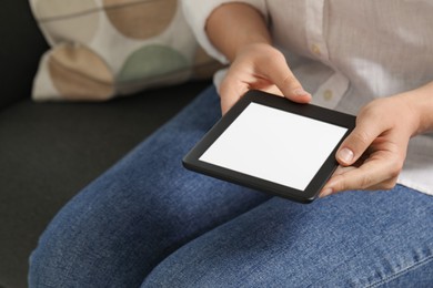 Young woman using e-book reader on sofa, closeup. Space for text