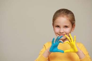 Photo of Little girl making heart with her hands painted in Ukrainian flag colors on light grey background, space for text. Love Ukraine concept
