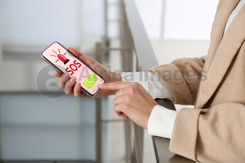 Woman holding smartphone with emergency call SOS on screen indoors, closeup