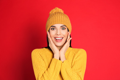 Excited woman wearing warm sweater and hat on red background. Winter season