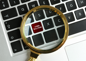 Magnifying glass and computer keyboard with phrase CYBER BULLYING on black button, top view 