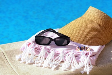 Photo of Blanket and beach accessories near outdoor swimming pool on sunny day, closeup