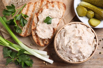 Photo of Lard spread served with bread and pickled cucumbers on wooden table, flat lay