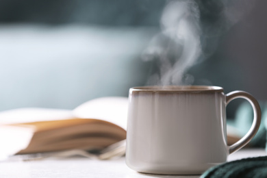 Cup of hot drink on white table against blurred background, space for text