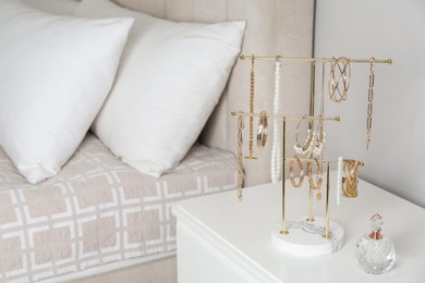 Holder with set of luxurious jewelry and perfume on nightstand in bedroom, space for text