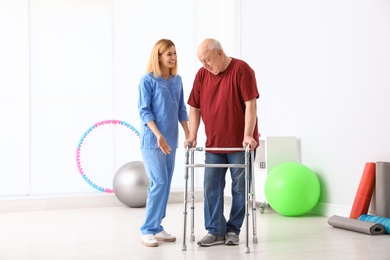 Caretaker helping elderly man with walking frame indoors