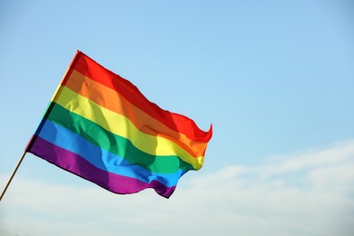 Bright LGBT flag against blue sky with clouds, space for text