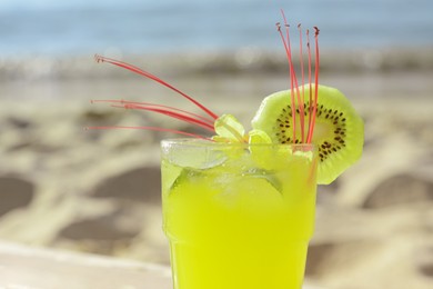 Glass of refreshing drink with kiwi and mint near sea, closeup