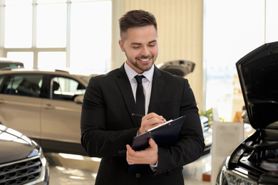 Photo of Young salesman with clipboard in modern car salon