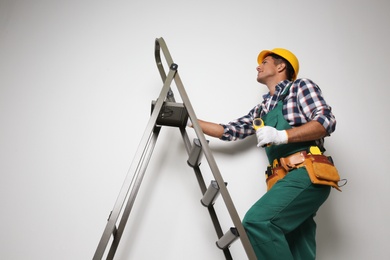 Professional builder climbing up metal ladder on light background