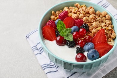 Bowl with tasty granola and berries on light grey table, closeup. Healthy meal