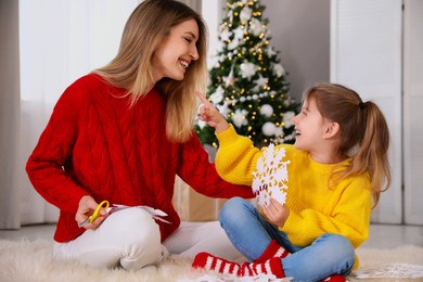 Happy mother and daughter with paper snowflake near Christmas tree at home