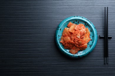Photo of Plate of spicy cabbage kimchi and chopsticks on black wooden table, flat lay. Space for text