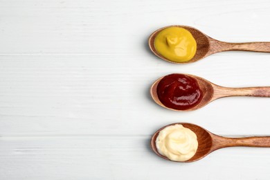 Ketchup, mayonnaise and mustard in spoons on white wooden table, flat lay. Space for text