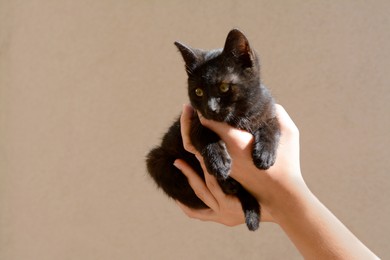 Photo of Woman holding black kitten against beige wall, closeup. Space for text