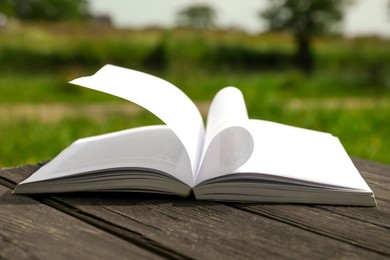 Photo of Open book on wooden table in countryside