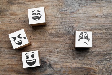 Photo of Cubes with sad and funny faces on wooden table, flat lay. Bullying concept