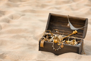 Photo of Open wooden treasure chest on sand, space for text