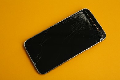 Smartphone with cracked screen on orange background, top view. Device repair