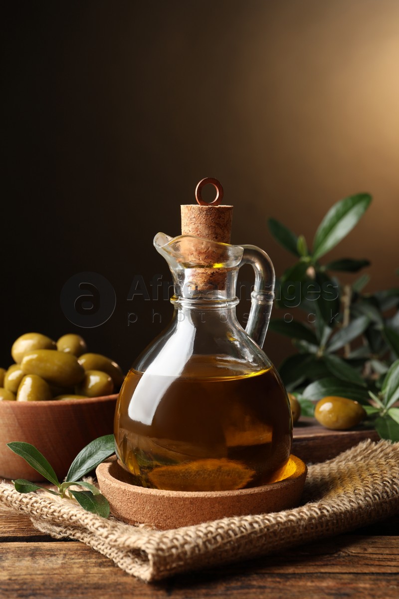 Glass jug of oil, ripe olives and green leaves on wooden table