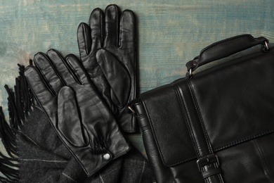 Stylish black leather gloves, bag and scarf on blue wooden table, flat lay