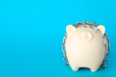 Piggy bank  with steel chain on light blue background, space for text. Money safety concept