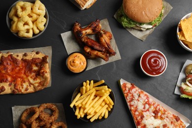 Photo of Burger, pizza and other fast food on black table, flat lay