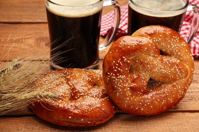 Tasty freshly baked pretzels, spikelets and mugs of beer on wooden table, closeup