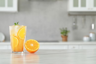 Photo of Tasty refreshing drink with orange on white marble table in kitchen. Space for text
